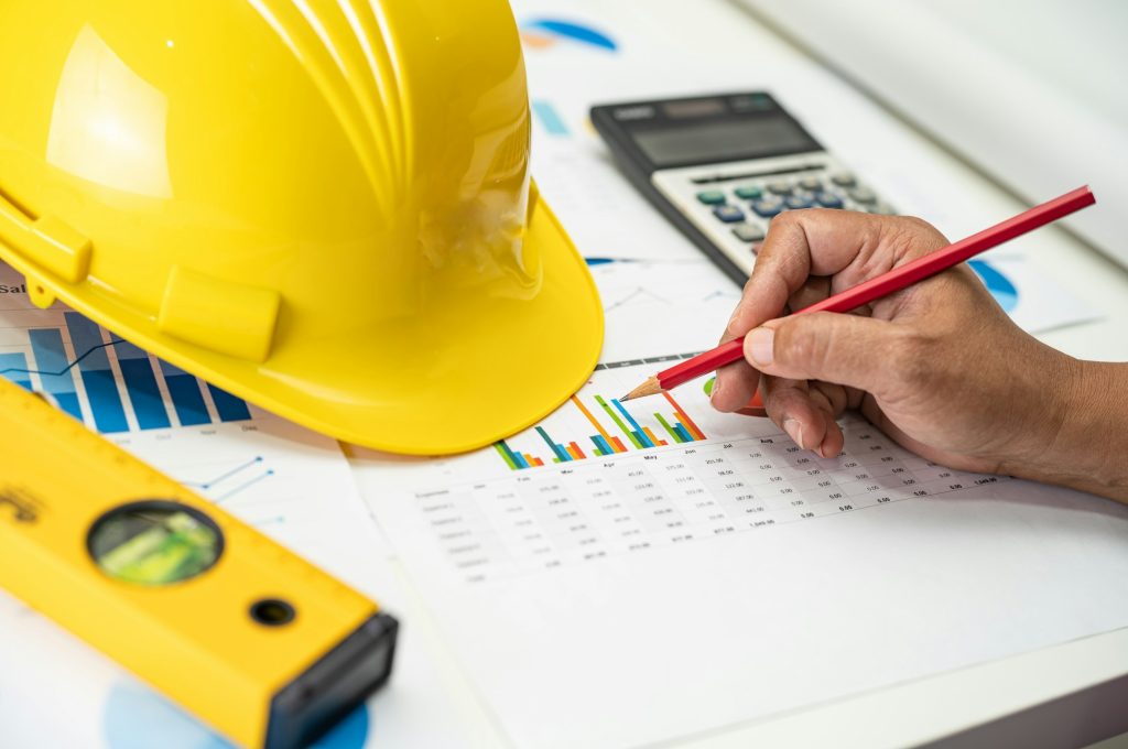 Asian engineer with plan project blueprint, graph and yellow helmet and engineering