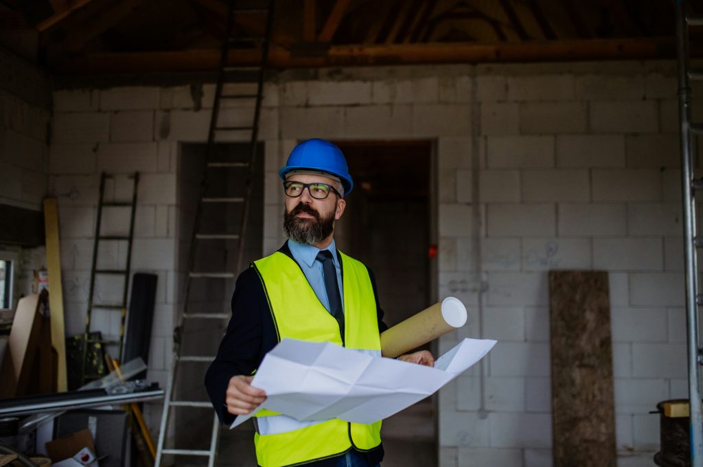 Mature businessman controlling blueprints from unfinished house.