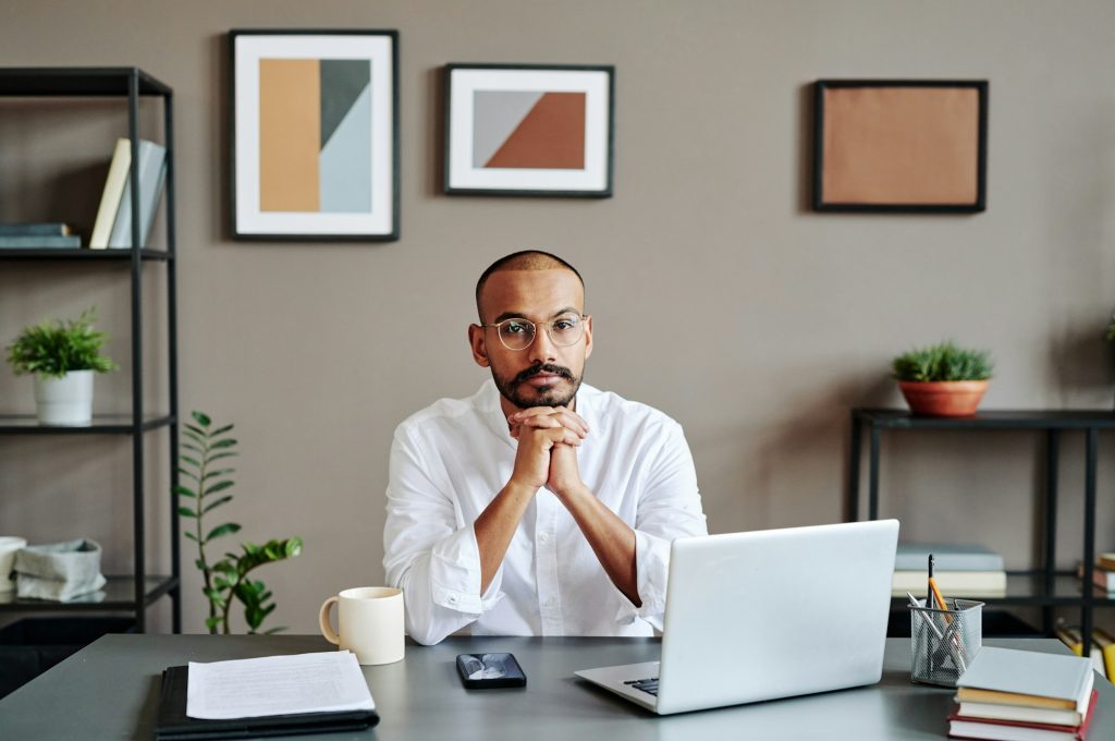 Young serious Muslim businessman in white shirt sitting by workplace
